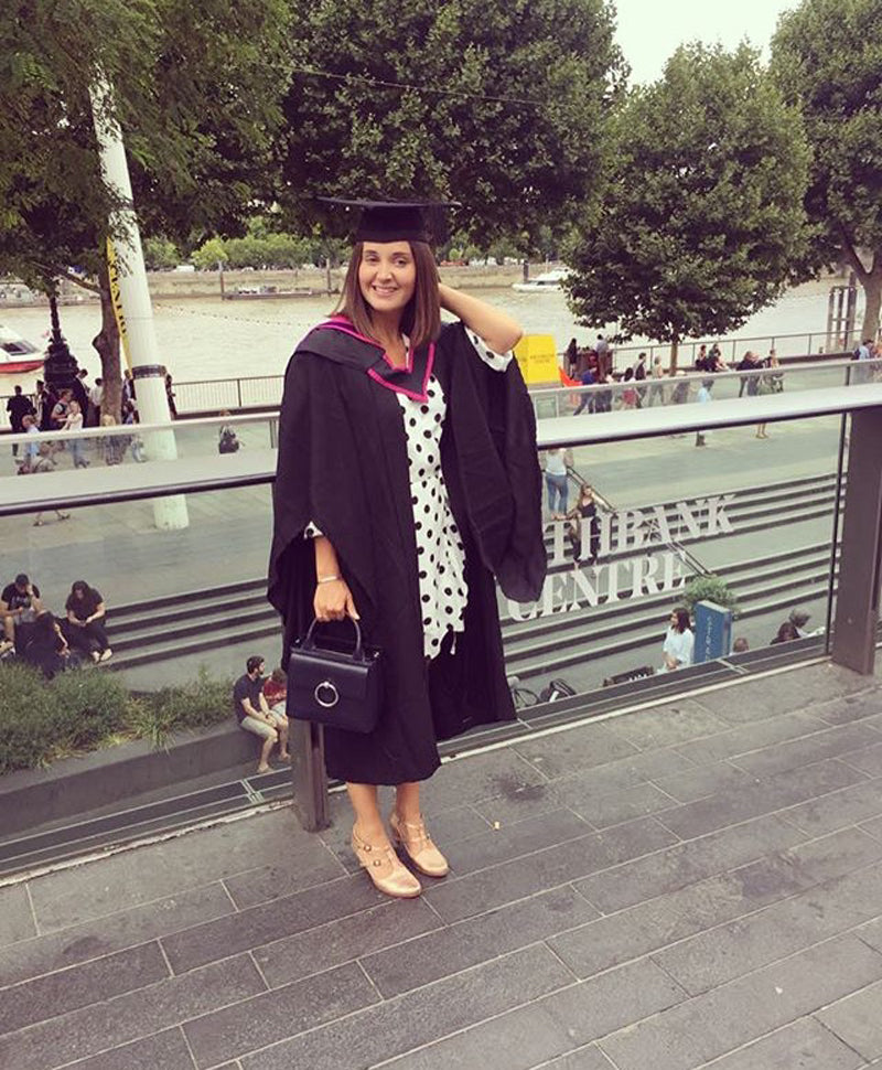 Girl at London's Southbank wearing graduation robes and hat, with designer Tracey Neuls gold High heels