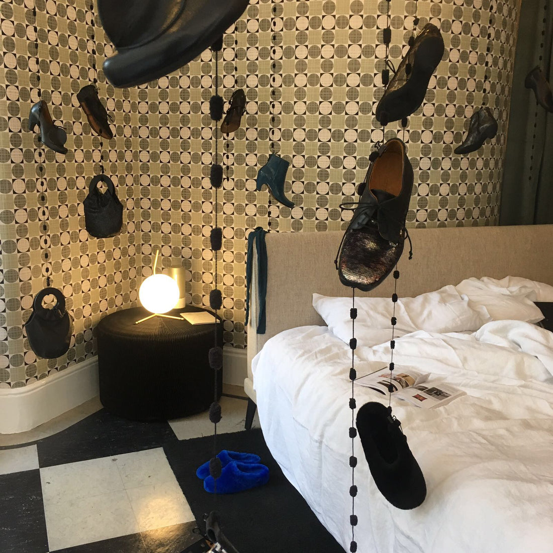 A bedroom interior in a shop with shoes hanging and a bedside lamp glowing