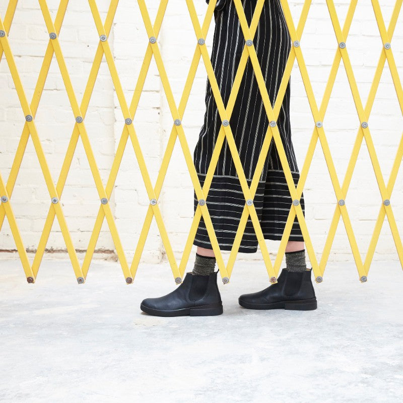 Woman seen through a yellow grid shutter wearing socks with chunky black Chelsea boots