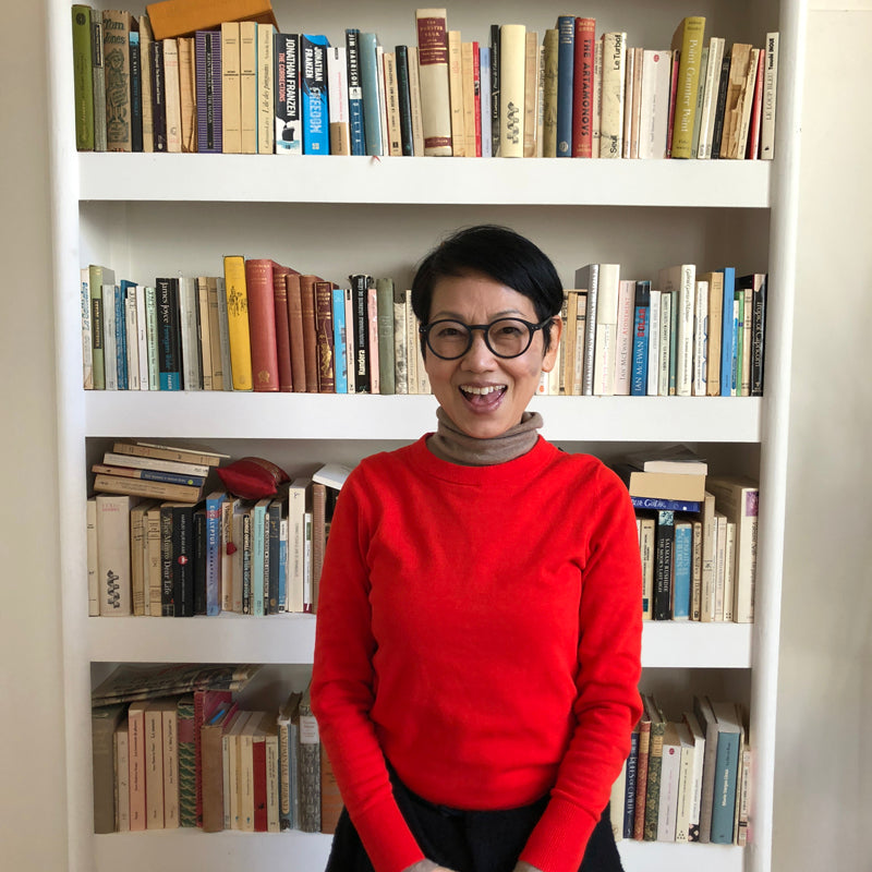 WOman from Hong Kong in red jumper stood in front of bookcase