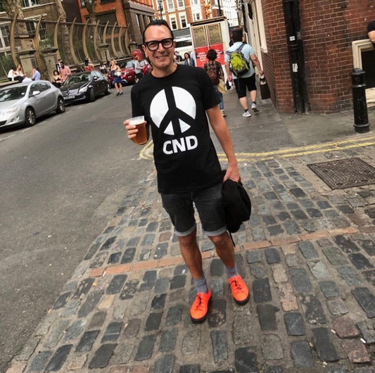 Man in CND t-shirt and bright orange trainers, holding a pint 