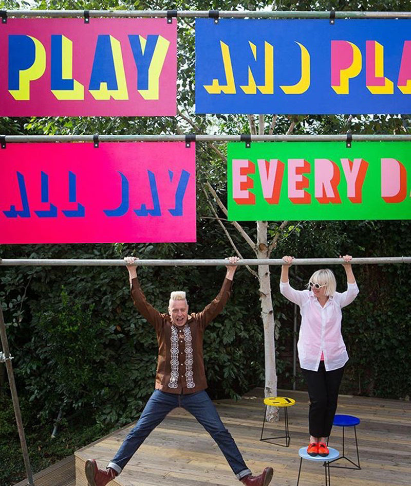 Designers hang off sign saying 'Play and play all day everyday' in bright colours