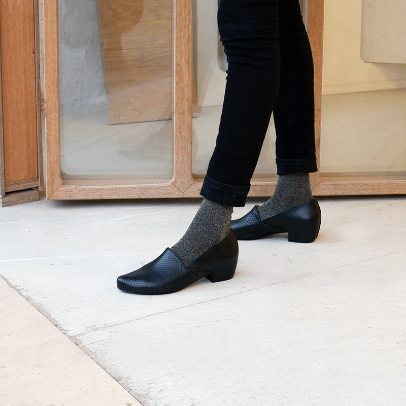 WOman's legs wearing black trousers and back mid heel slip on loafers and sparkly black socks