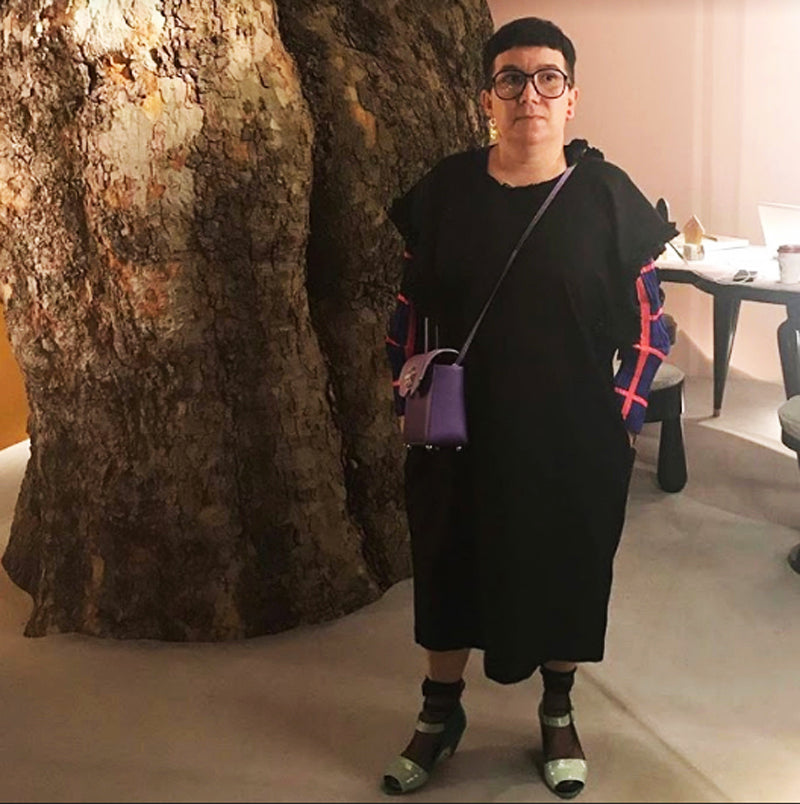 Jewellery curator Valery Demure, wearing colourful handbag and shoes in front of giant tree trunk